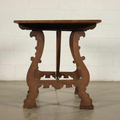 Mesa de caballete hecha con piezas antiguas, sostenida por patas onduladas y talladas, unidas por un travesaño, la parte superior del marco tiene un sello de inventario en la parte inferior.