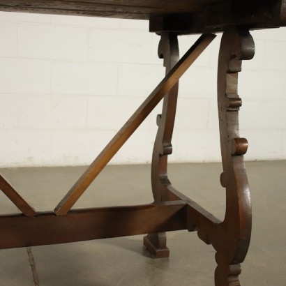 Mesa de caballete hecha con piezas antiguas, sostenida por patas onduladas y talladas, unidas por un travesaño, la parte superior del marco tiene un sello de inventario en la parte inferior.